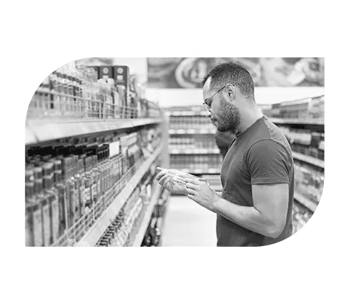 A man wearing glasses and a t-shirt is standing in a grocery store aisle, carefully reading a product label.