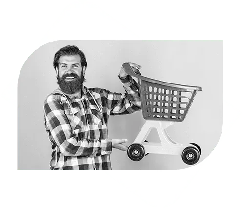 A bearded man in a plaid shirt smiles while holding and presenting a small plastic shopping cart.