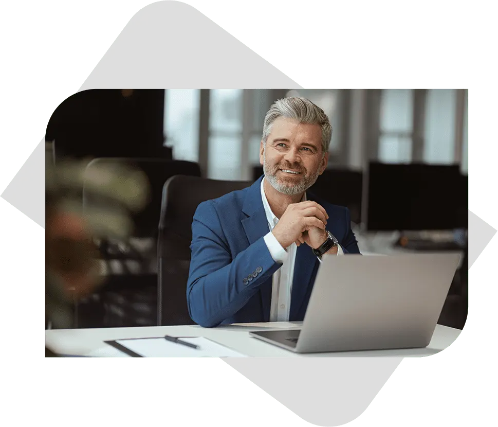 Smiling businessman in a blue suit working on a laptop at an office desk