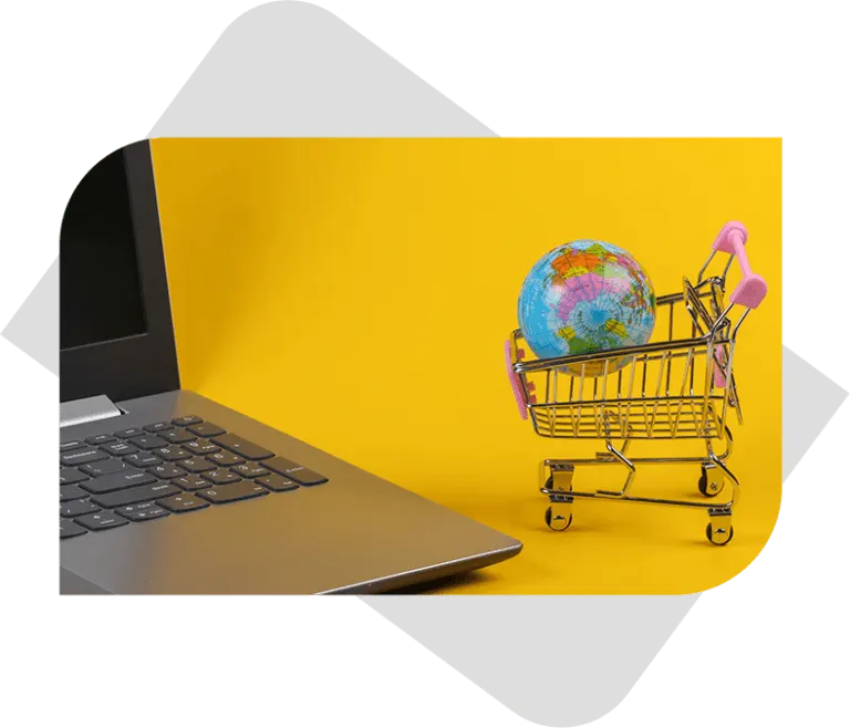 earth globe inside small Shopping cart next to a laptop with yellow background