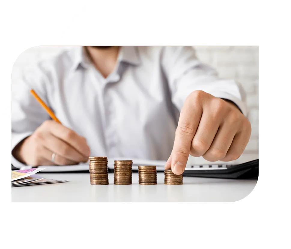 A man in a white shirt sits at a table, counting and stacking coins while writing on a piece of paper.